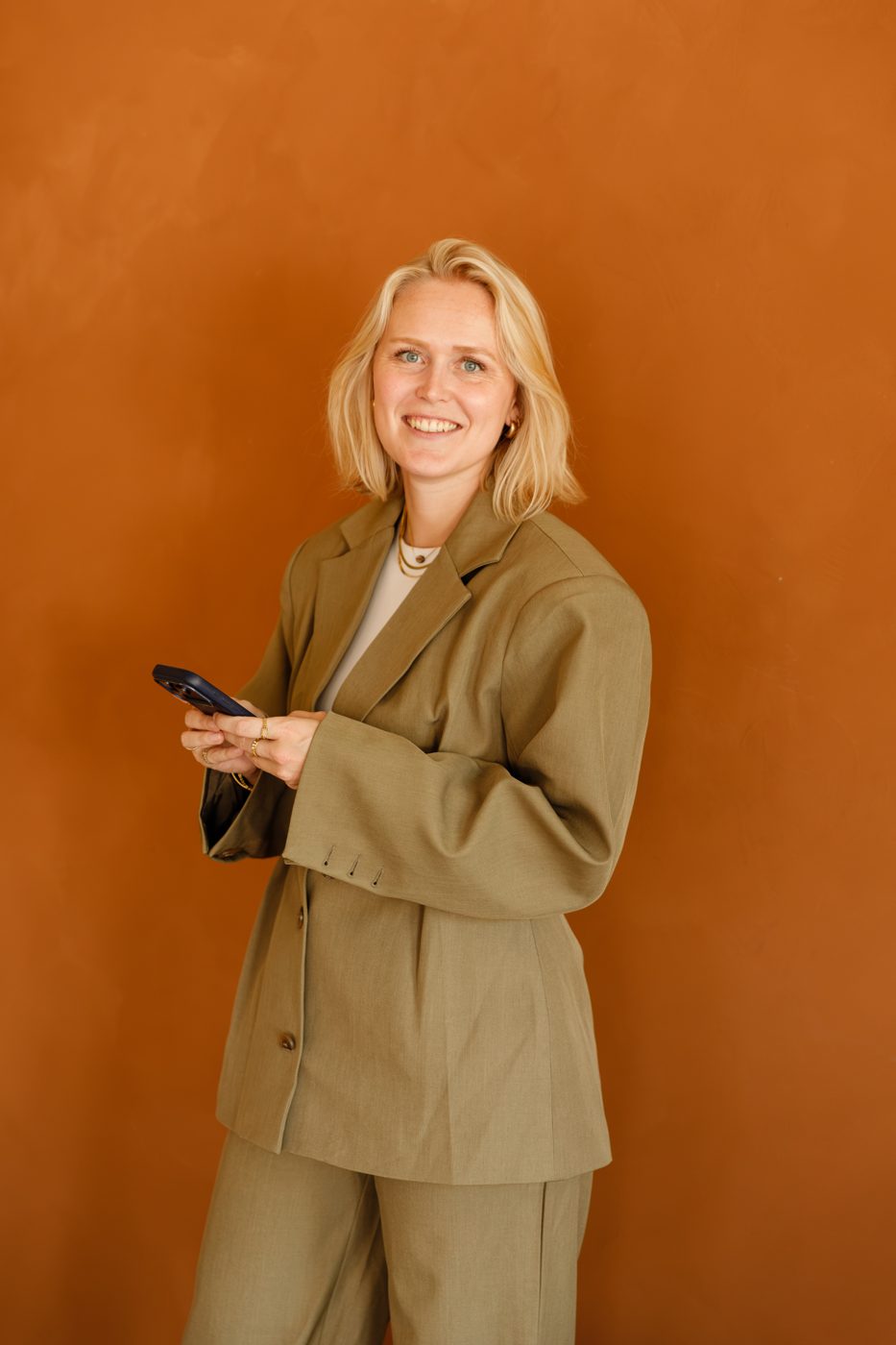 Jackie Donker voor een oranje muur, met haar telefoon in de hand