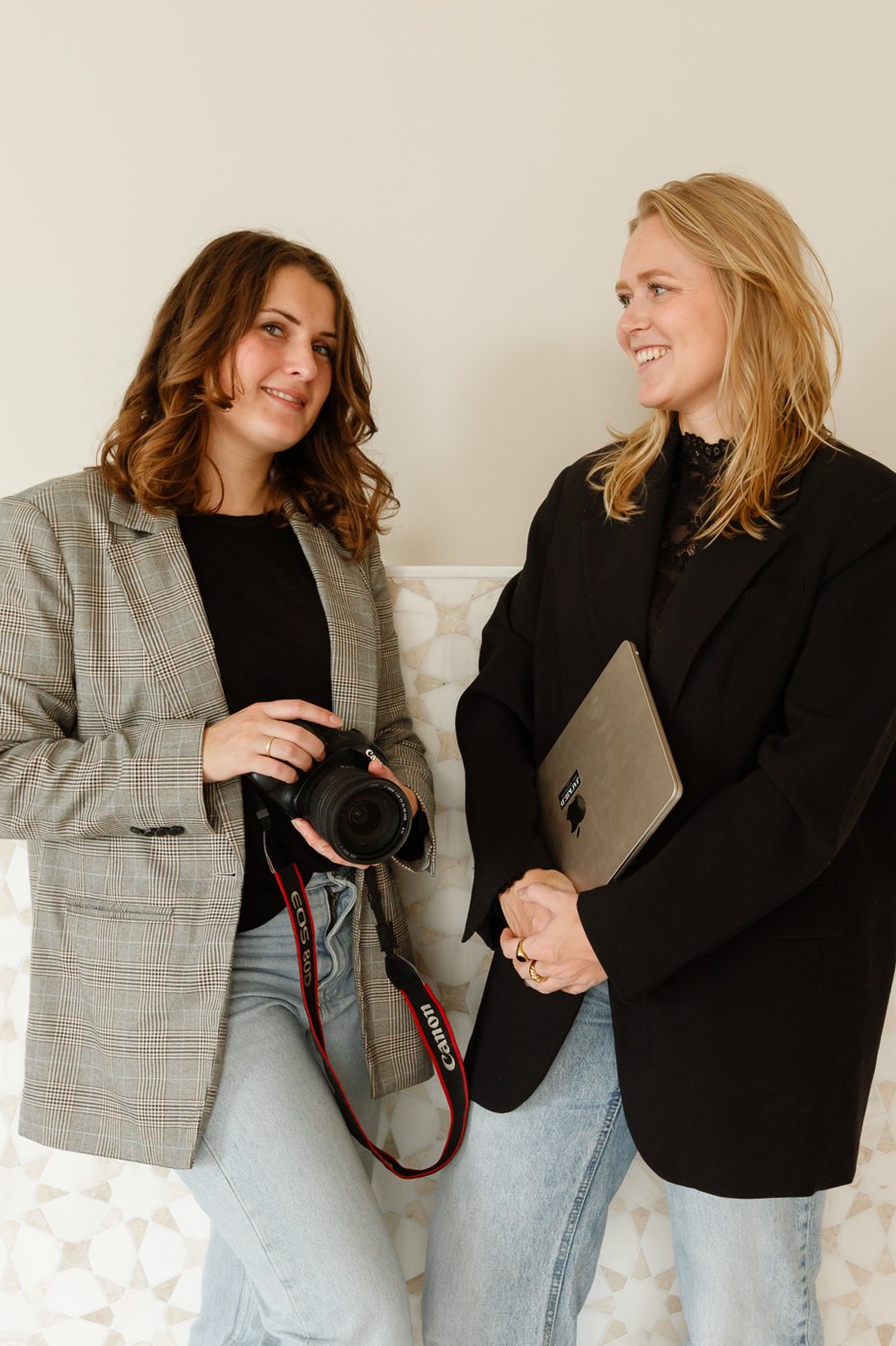 Fotograaf Cynthia met camera en Jackie met laptop, lachend naast elkaar